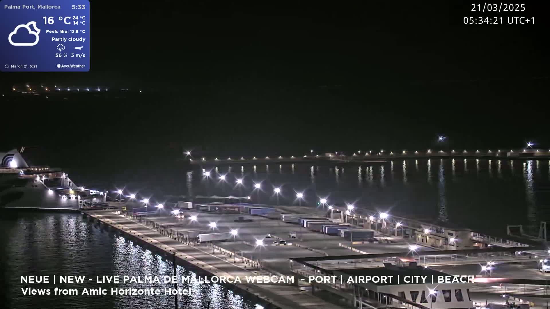 A partly cloudy night scene shows a cruise ship docked at a port with numerous trucks and cars parked on the dock, illuminated by lights reflecting on the calm water.