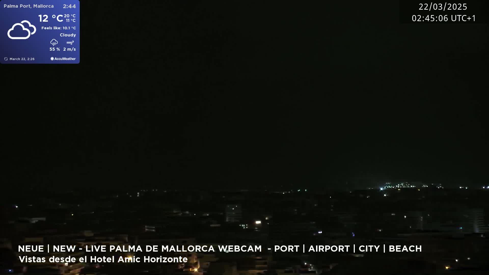 A nighttime, cloudy view of a city illuminated by scattered lights under a dark sky.