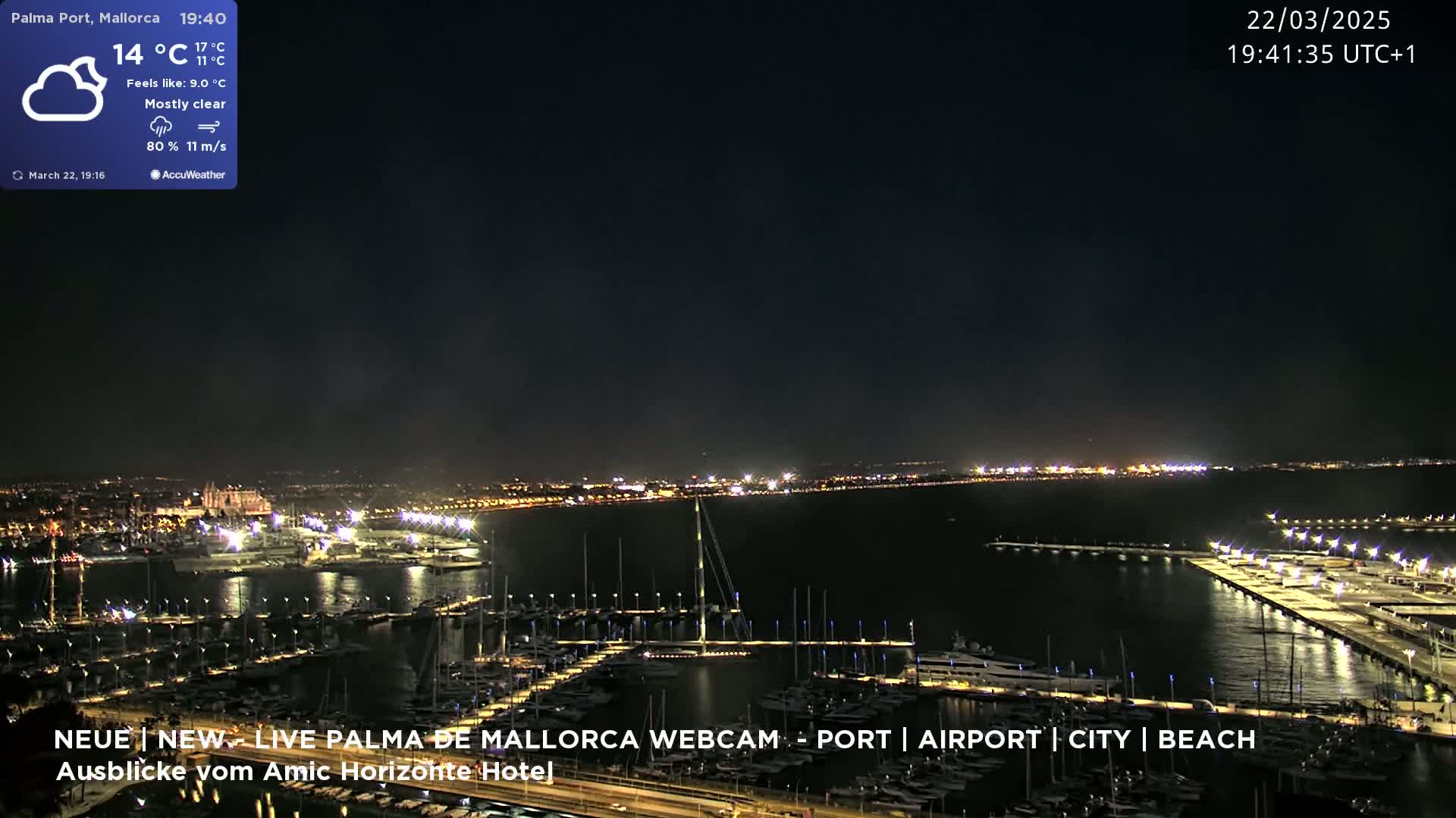 A nighttime, mostly clear view of a harbor filled with boats, with a city skyline and lights visible in the distance.