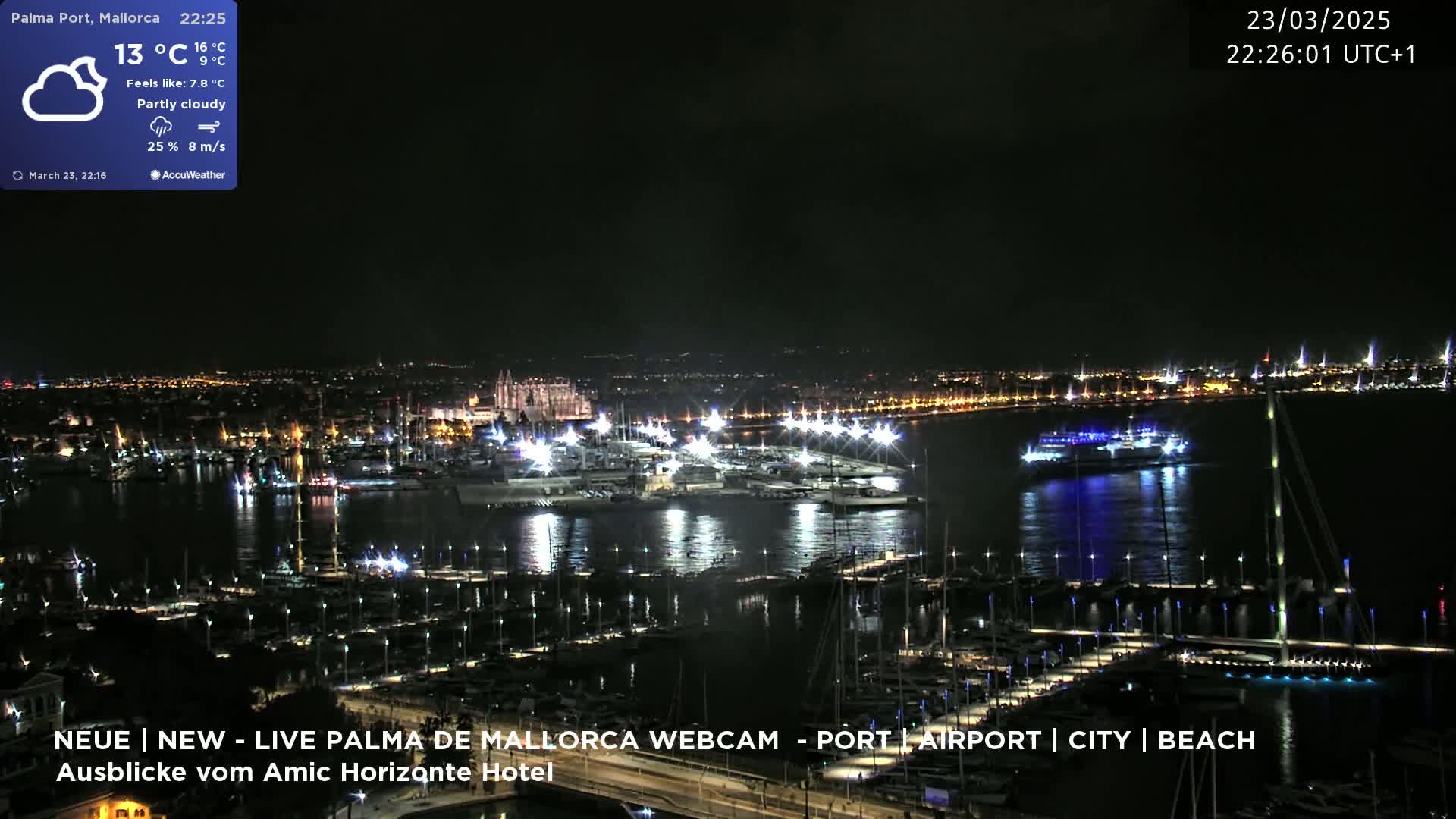 A nighttime, partly cloudy view of a harbor filled with boats, a city skyline, and a large building in the distance.