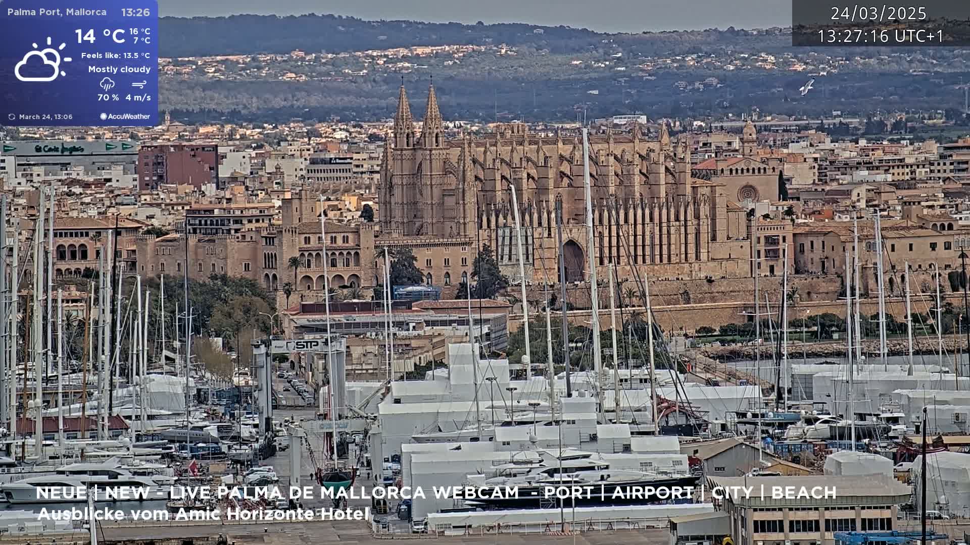 A mostly cloudy day in a harbor city, showing a large cathedral and many sailboats docked at a marina.