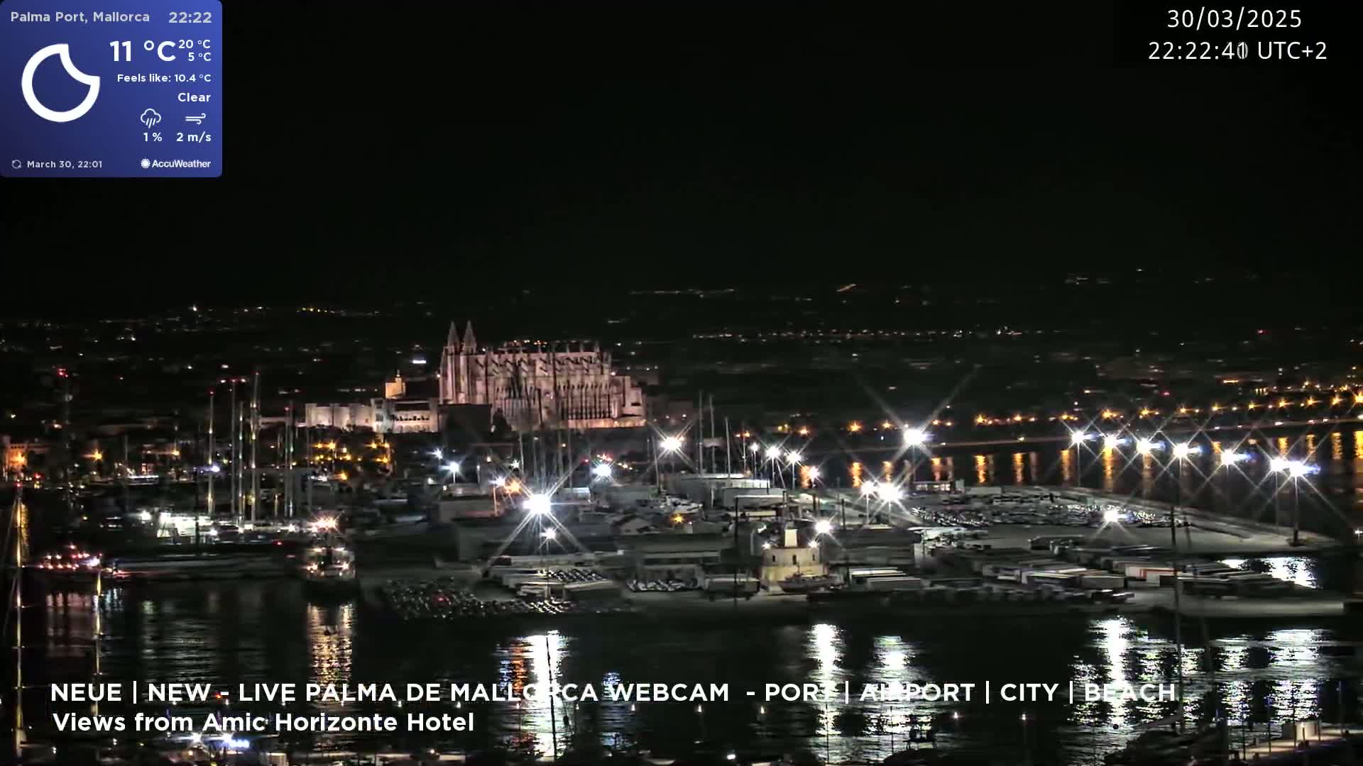 A nighttime harbor scene with a large, illuminated cathedral in the background under clear skies.
