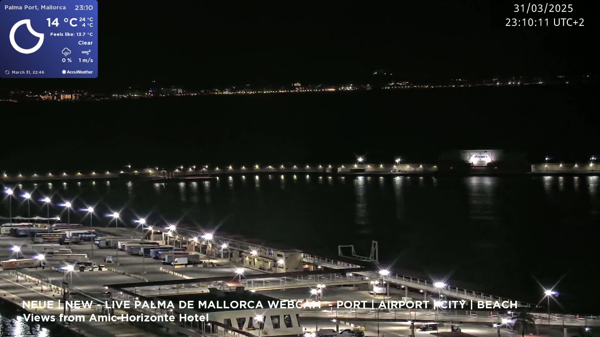 A nighttime view of a harbor with a calm body of water reflecting city lights, under a clear sky.