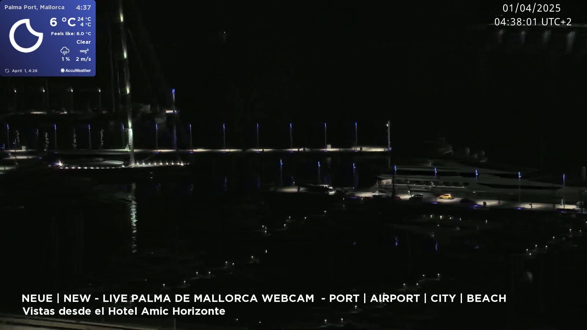 A nighttime view of a marina with many boats, lit by lights along a dock, under clear skies.