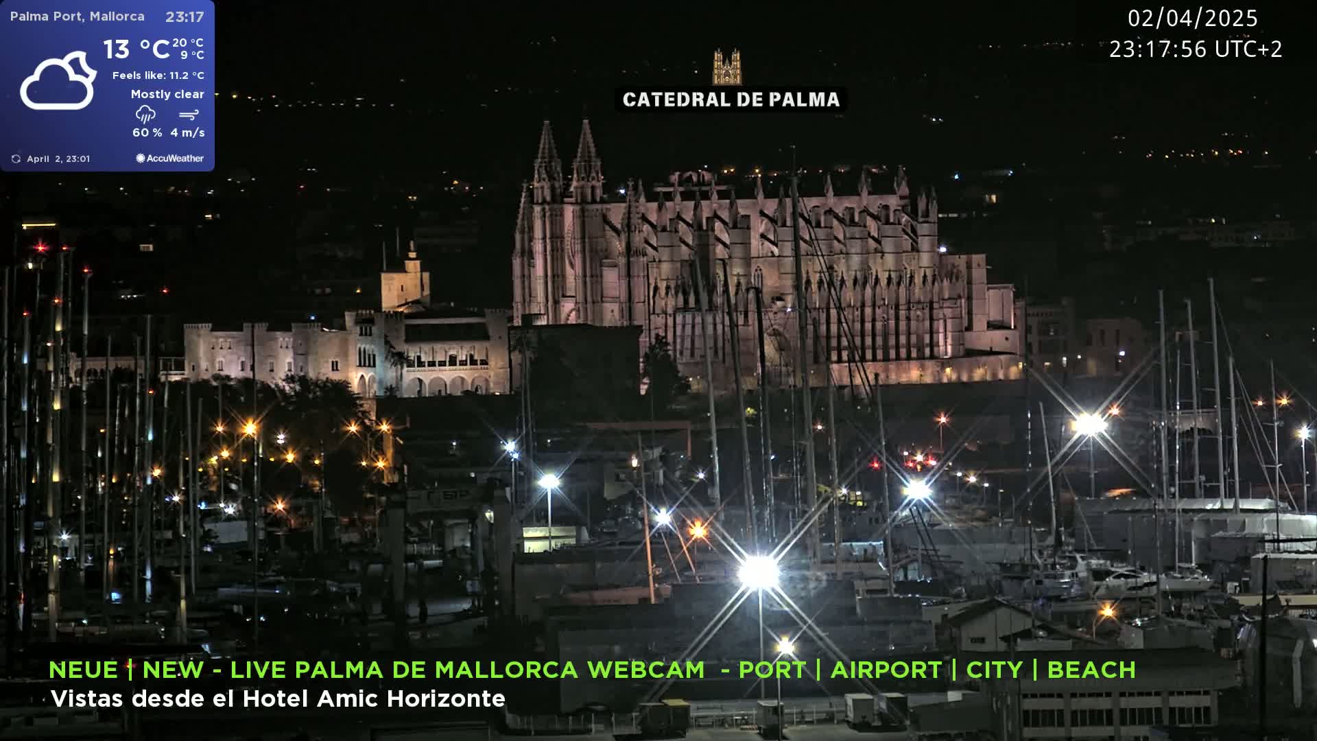 A nighttime harbor scene shows a large illuminated cathedral in the background, with many boats and lights illuminating the marina under mostly clear skies.