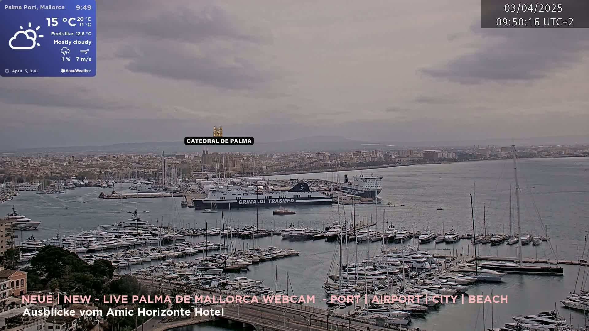 A mostly cloudy harbor scene shows numerous yachts and boats docked, with a large ferry in the background, and a city skyline visible under an overcast sky.
