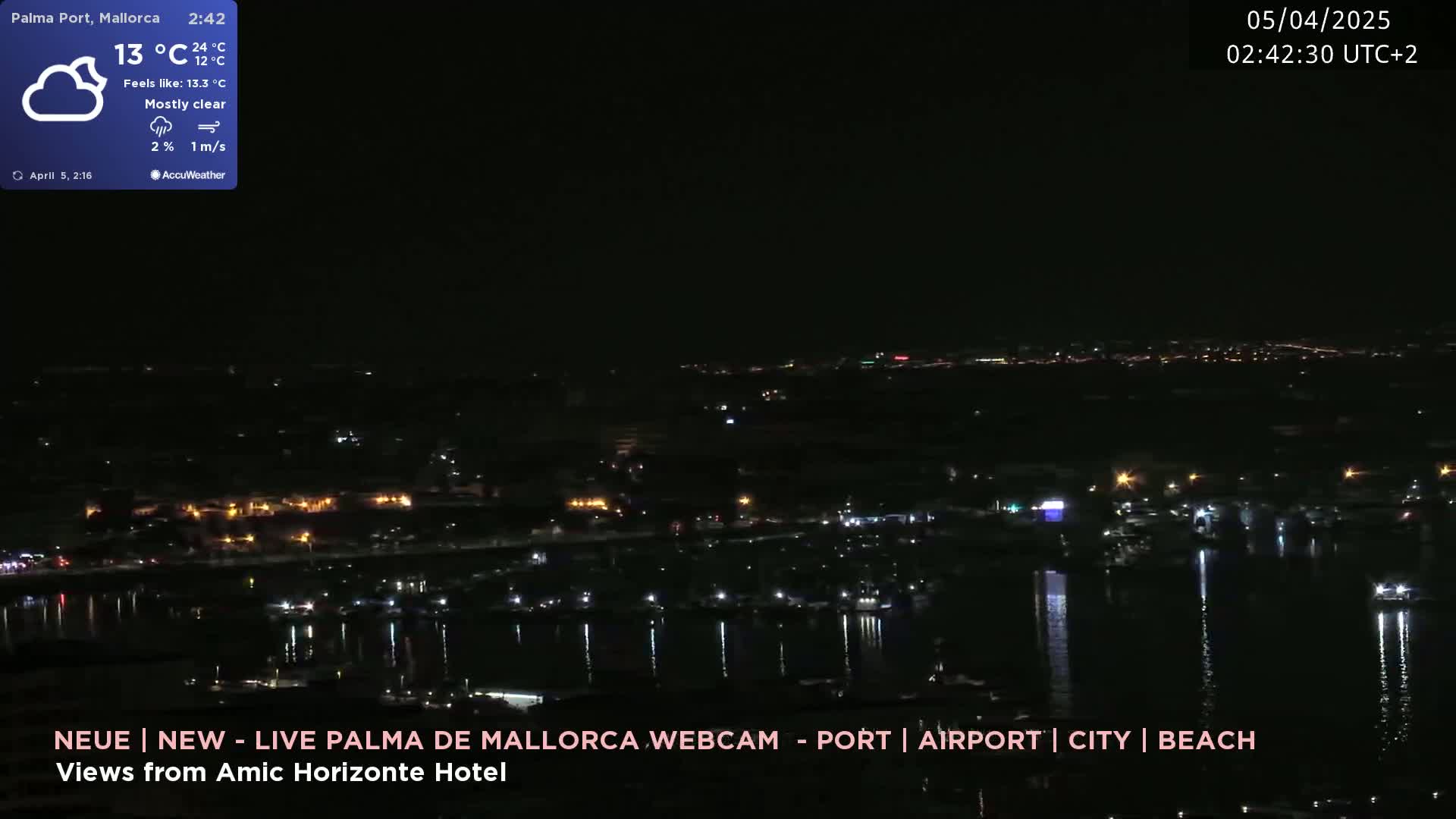 A nighttime, mostly clear view of a city harbor and coastline with lights reflecting on the water.