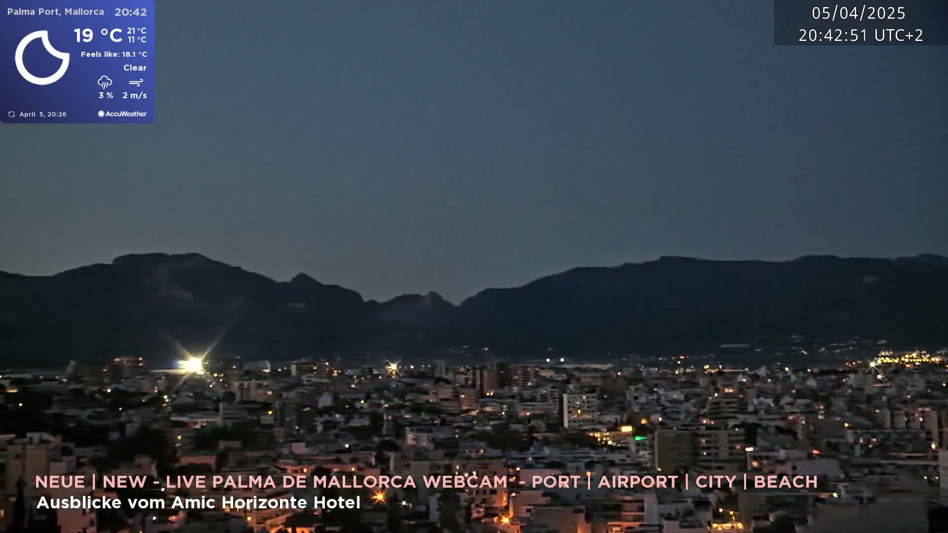 A nighttime view of a city illuminated by lights, with dark mountains in the background under a clear sky.