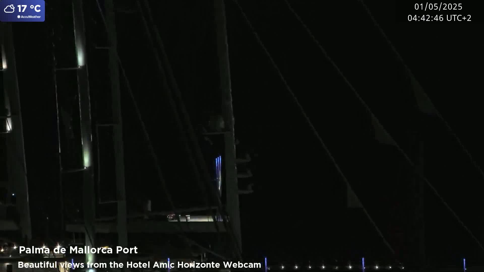 A nighttime view of a port, showing the masts of several boats illuminated by artificial lights, under a clear sky.