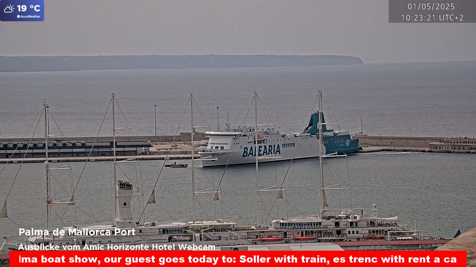A ferry and several large sailing vessels are docked in a harbor on a hazy day.