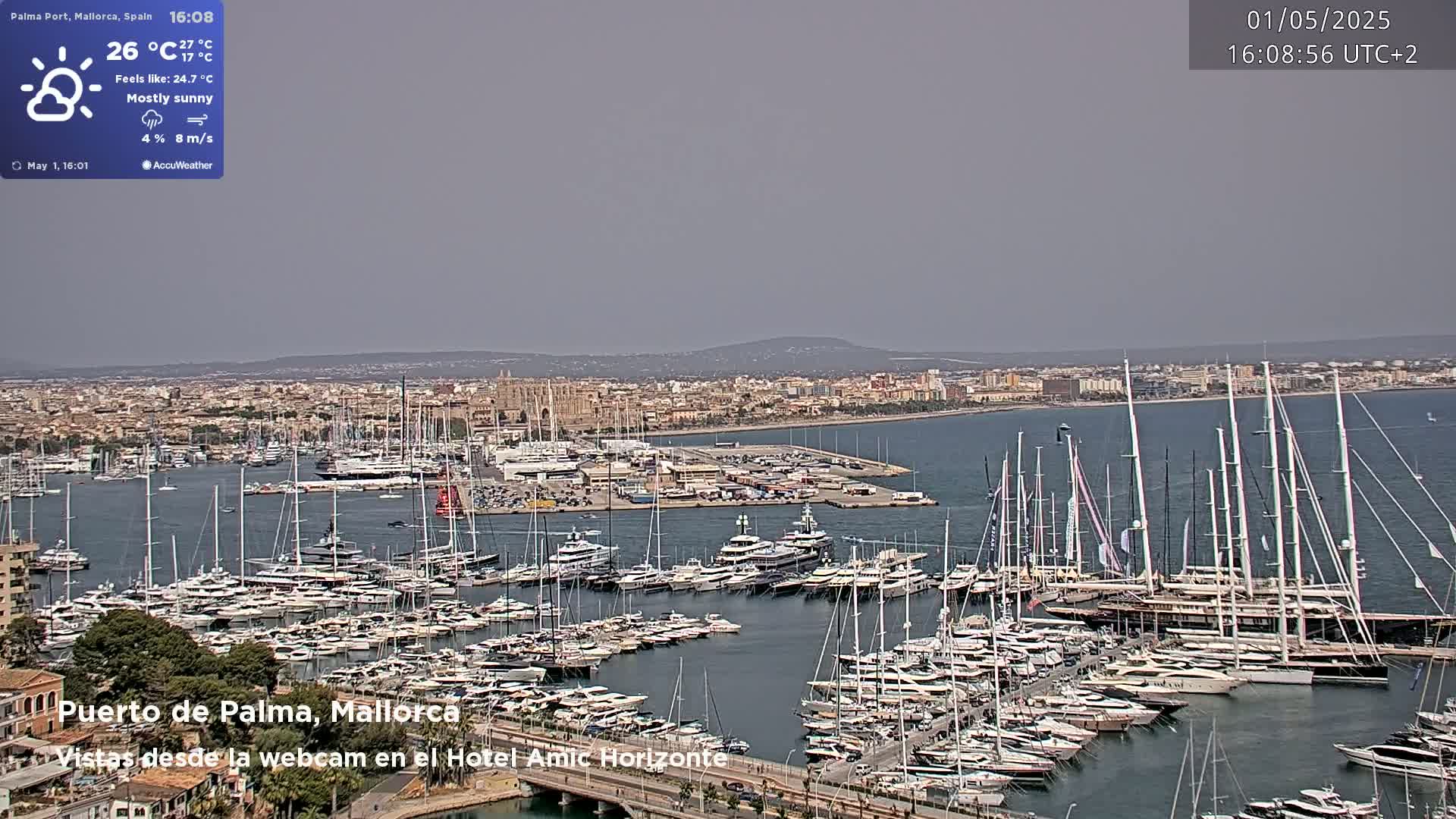 A mostly sunny harbor filled with many sailboats and yachts, with a city visible in the background.