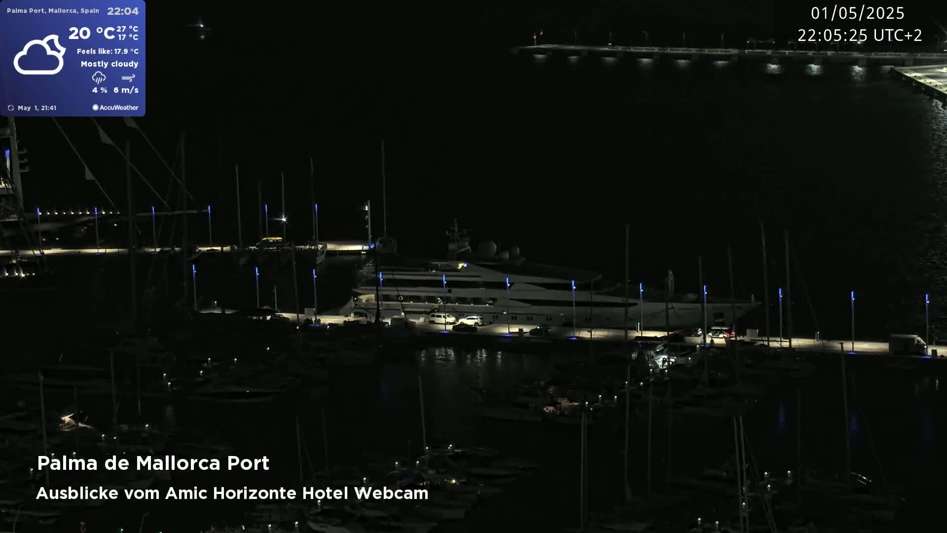 A mostly cloudy night scene shows a marina with many docked boats and a large yacht at a pier, illuminated by lights.