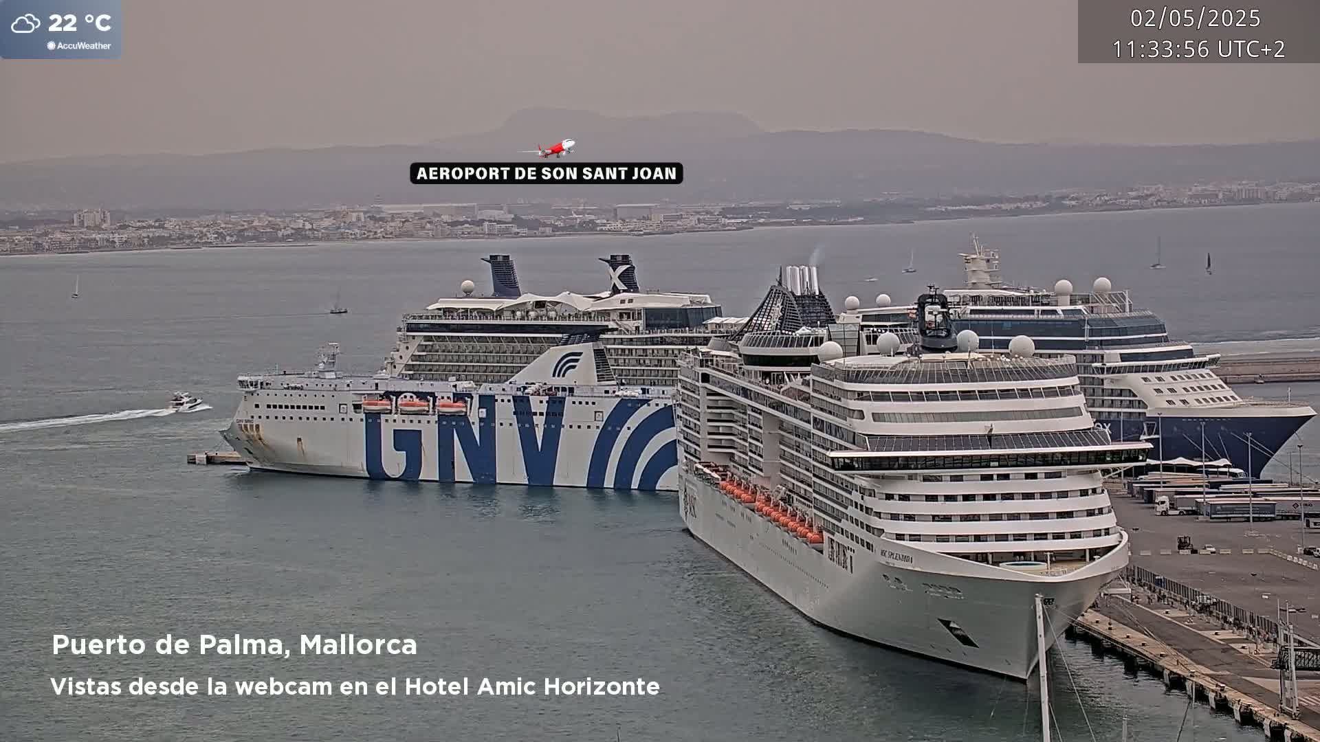Three large cruise ships and a ferry are docked at a port on an overcast day, with a hazy view of a distant city and mountains.