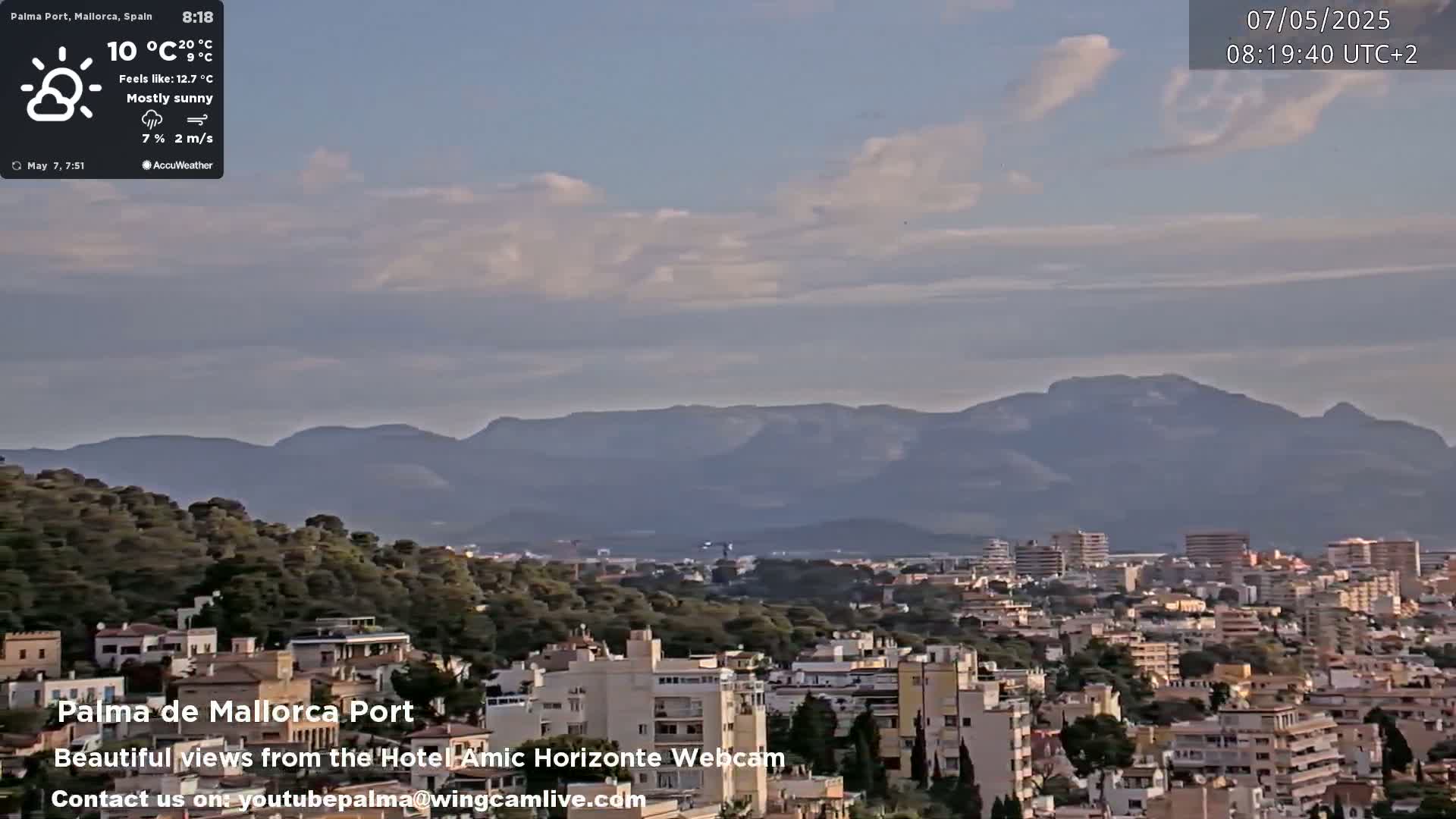 A mostly sunny cityscape with a mountain range in the background.