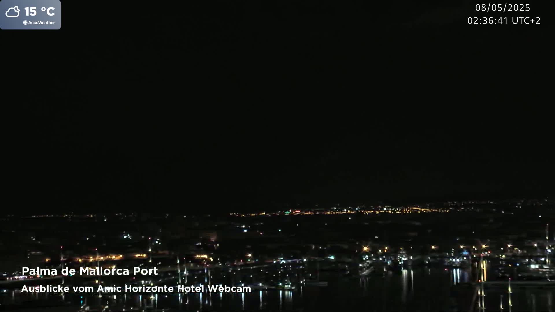 A nighttime view of a harbor town with scattered lights, under a mostly clear sky at 15°C.