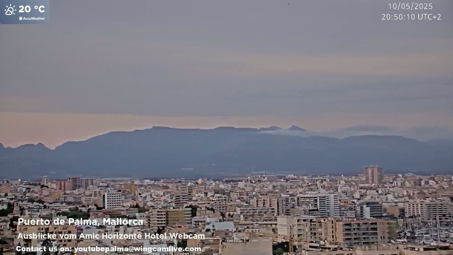 A sprawling city with numerous buildings extends to a range of distant mountains under a hazy, light-grey sky.