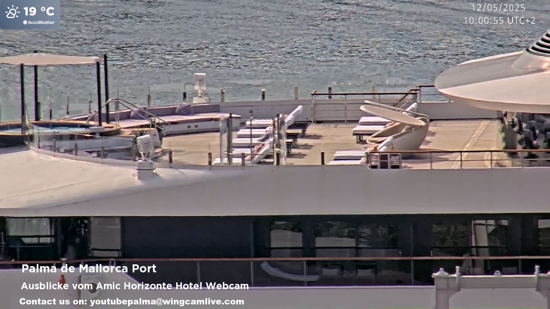A ship's sun deck with lounge chairs, a hot tub, and an umbrella, overlooking calm water on a partly sunny 19°C day.