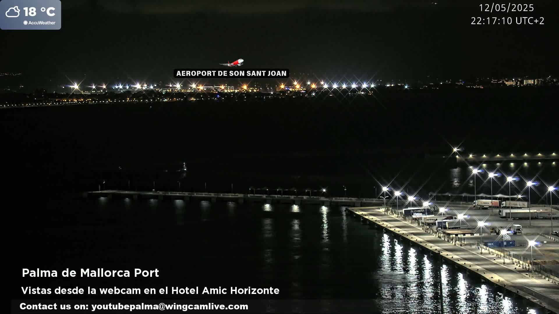 A nighttime view of a brightly lit port and a distant airport, with calm water reflecting the lights.