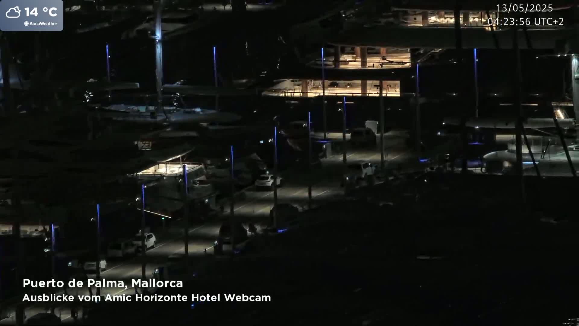An aerial nighttime view of a marina with boats and cars parked along a road, under a clear sky at 14°C.