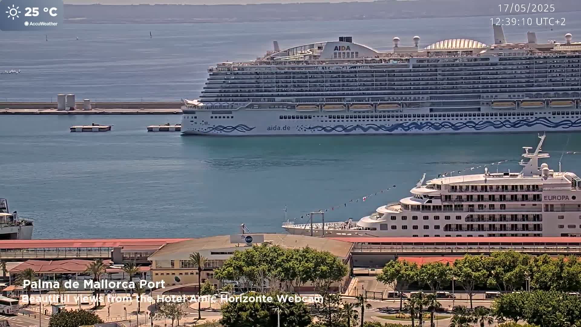 Two cruise ships are docked at a port on a sunny day with calm water.