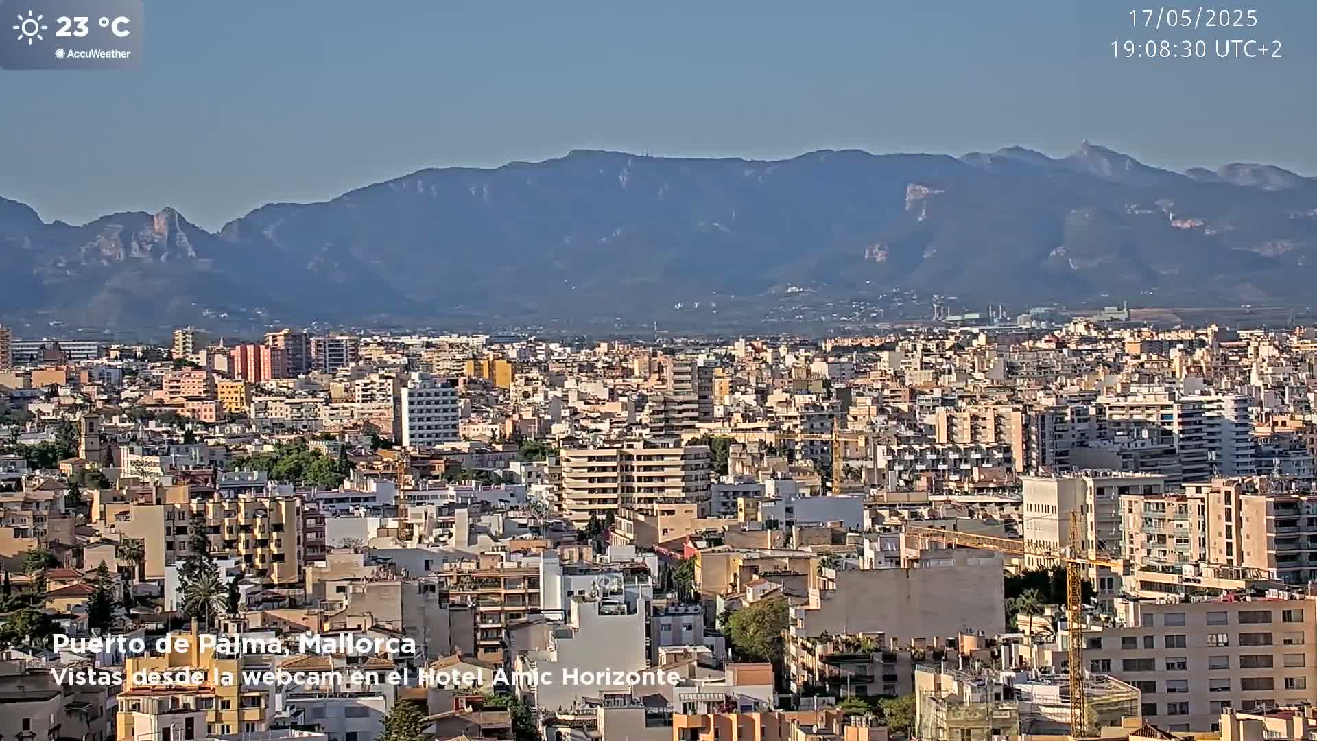A sprawling city, bathed in sunlight, extends to a range of distant mountains under a clear sky.