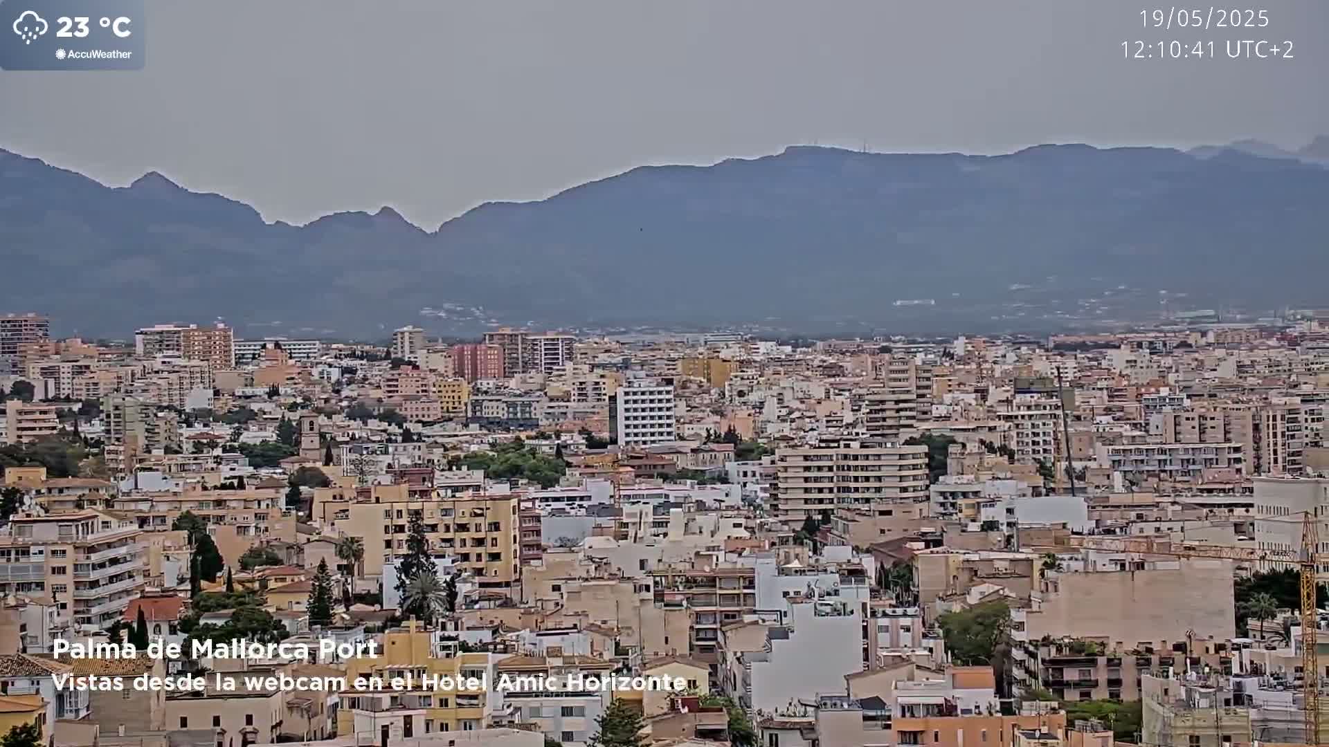 A hazy view of a densely populated city, nestled beneath a range of distant mountains, on a 23°C day.