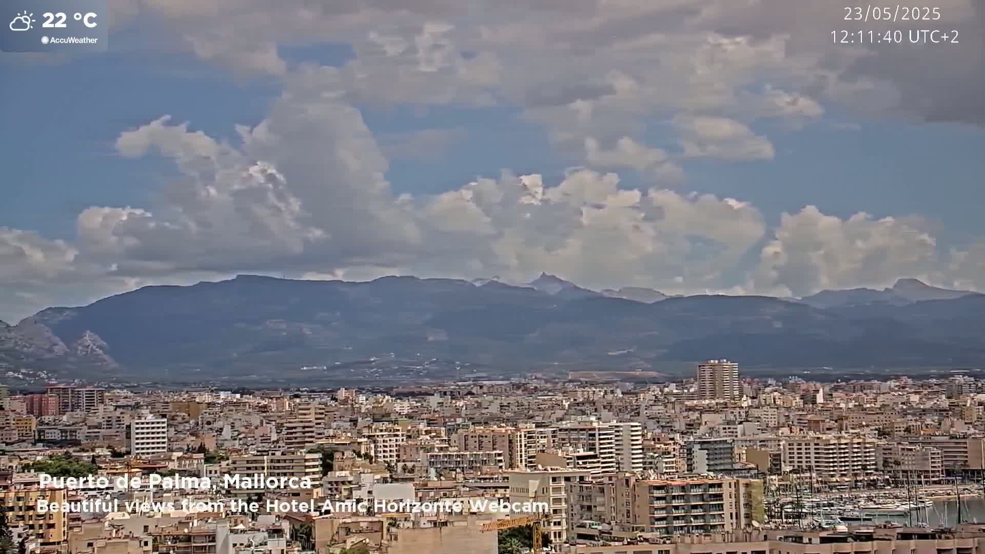 A partly cloudy day reveals a sprawling city with a mountain range in the background.