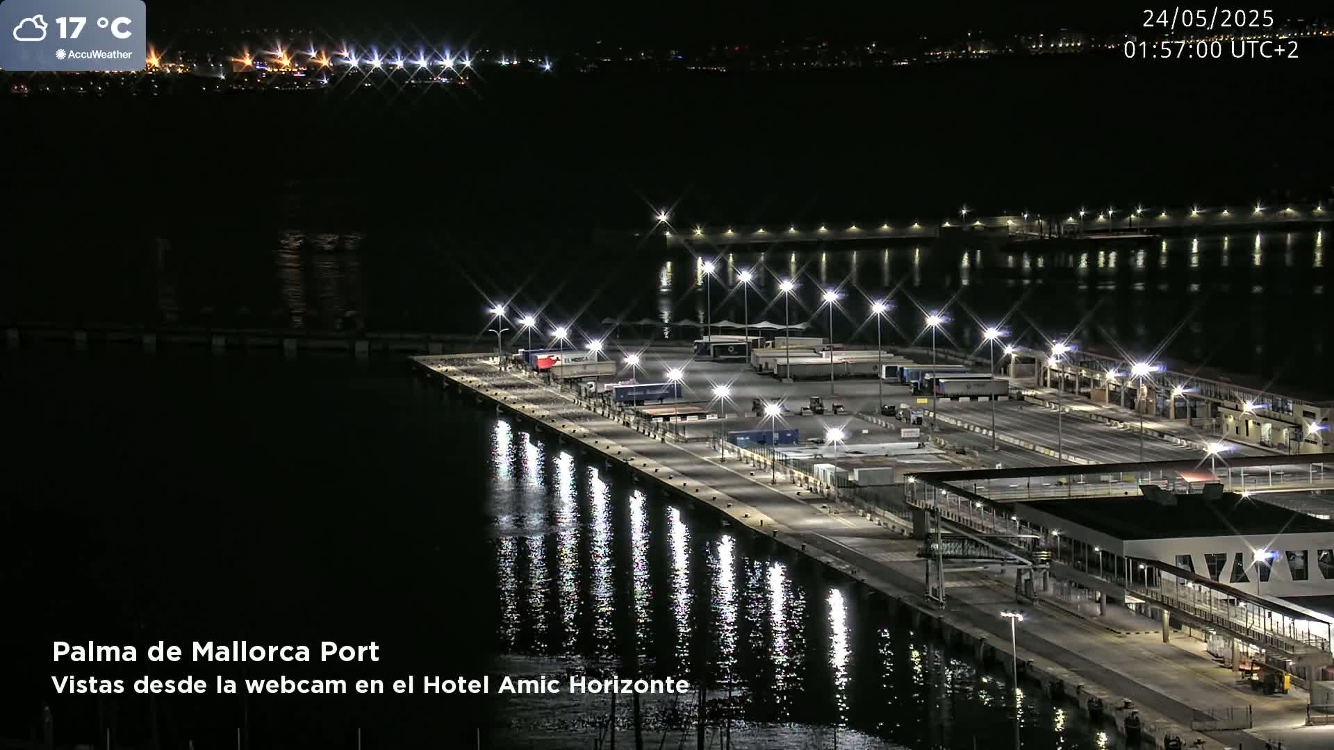 A brightly lit port at night, reflecting in calm water under a partly cloudy sky.