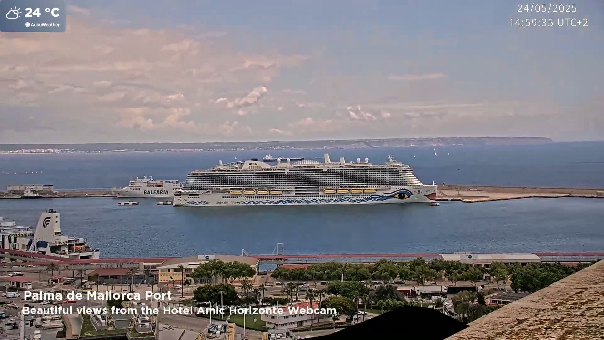 A large cruise ship is docked in a harbor on a partly cloudy day with a temperature of 24 degrees Celsius.
