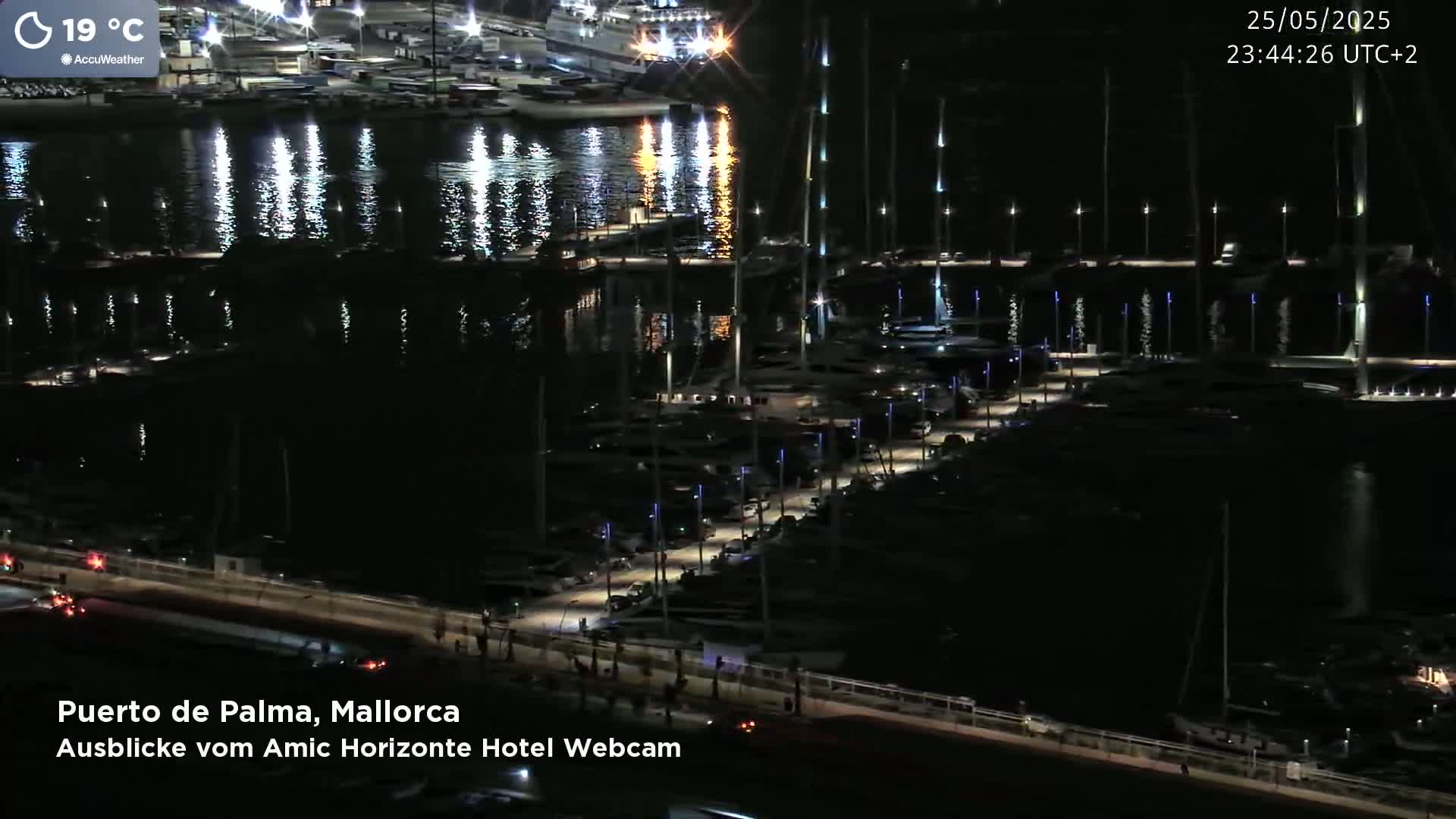 A nighttime view of a marina filled with boats, illuminated by lights along a walkway, under a clear sky.