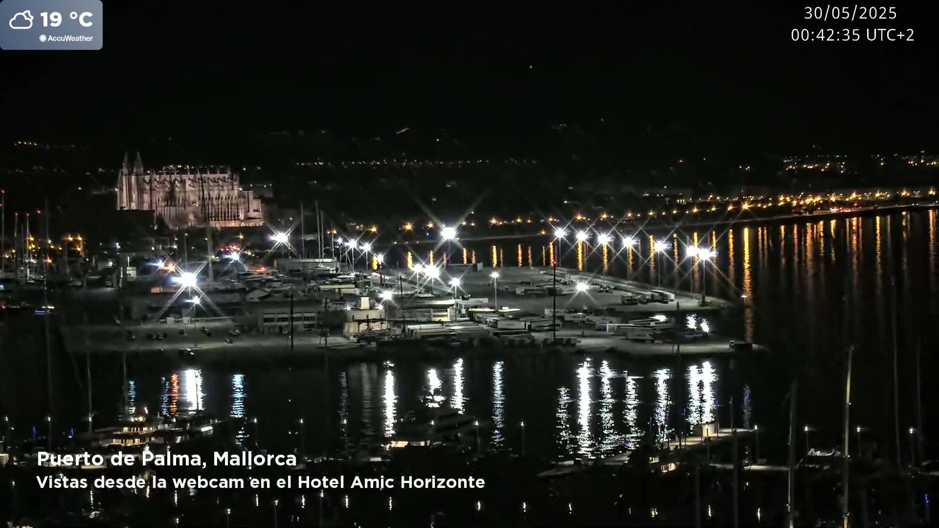 A nighttime harbor scene with a large illuminated building in the background and many boats and lights reflecting on the calm water.