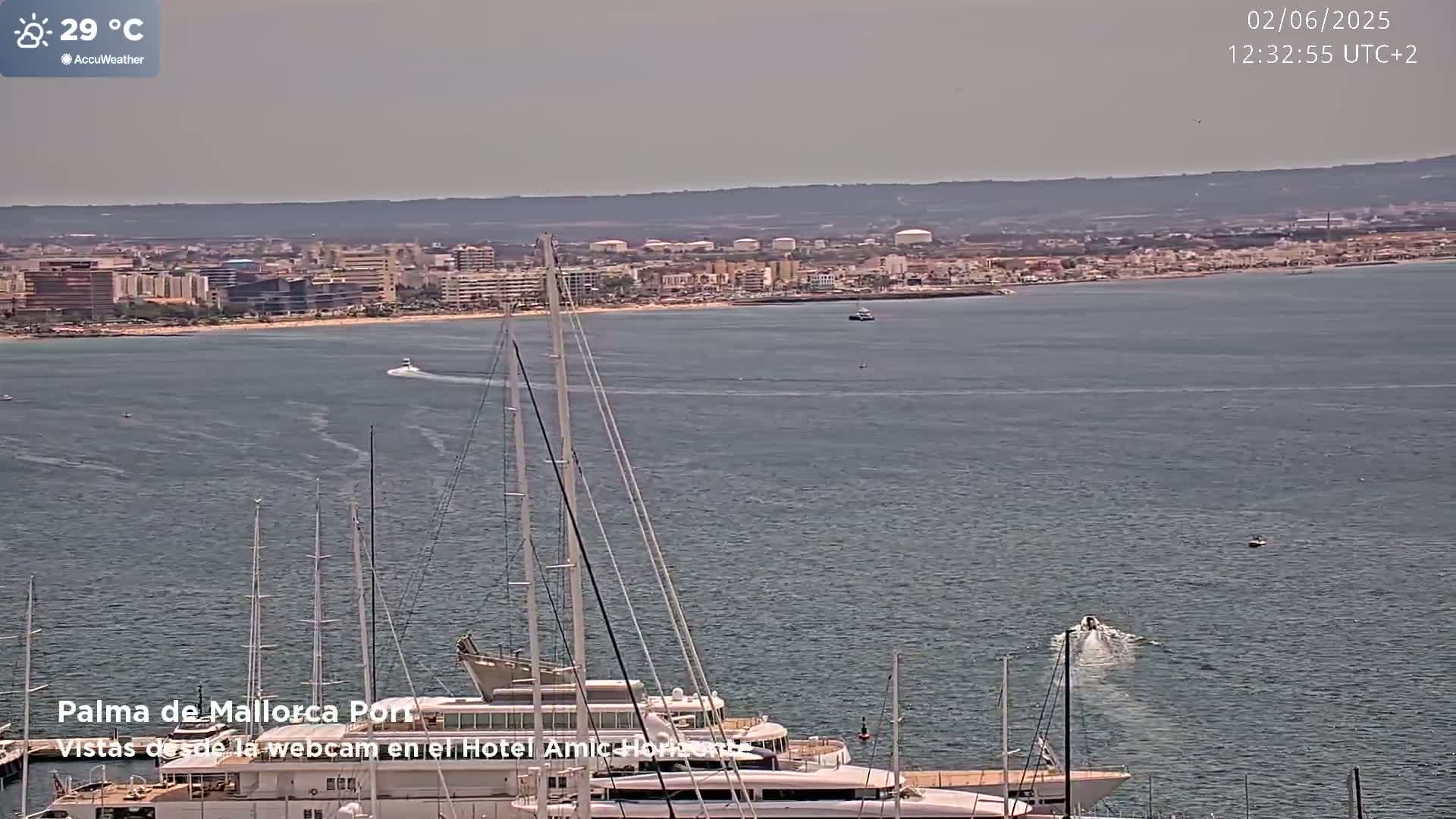 A harbor filled with sailboats is shown in front of a city on a partly sunny day with a temperature of 29 degrees Celsius.