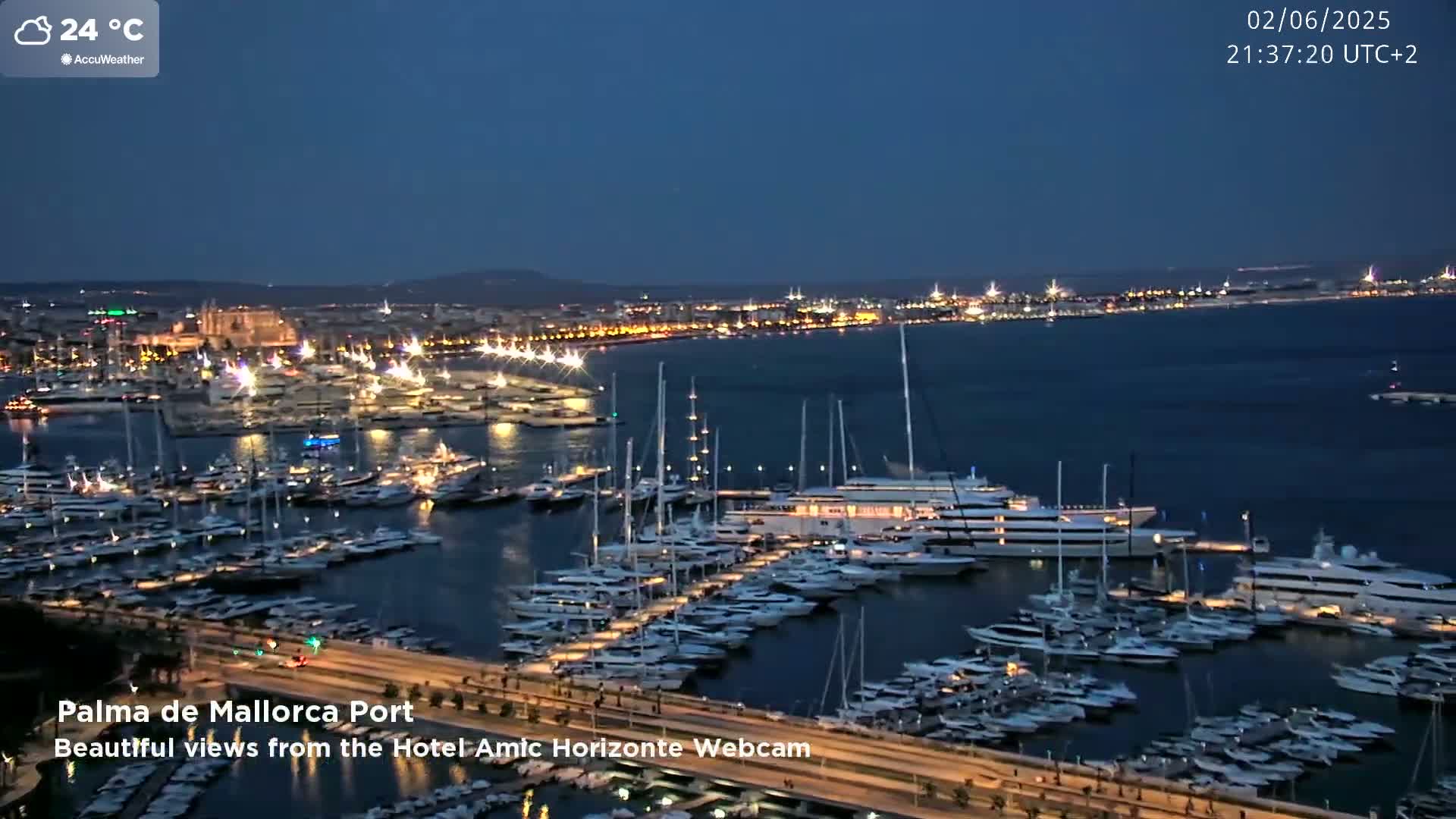 A nighttime, illuminated harbor filled with many yachts and boats under a clear, dark blue sky.