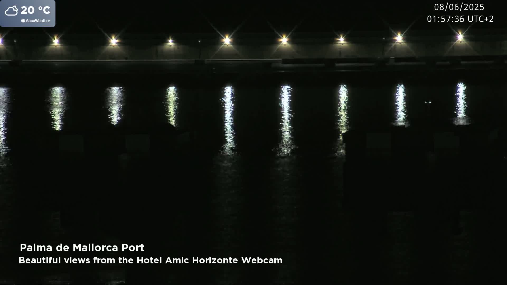 Lights on a structure at night illuminate the dark water below, reflecting in vertical streaks.