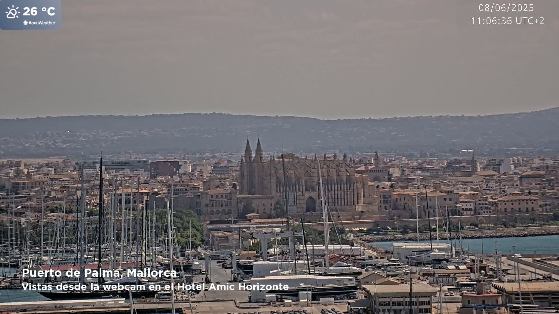 A hazy, sunny day reveals a harbor full of sailboats and a large cathedral overlooking a city in the distance.