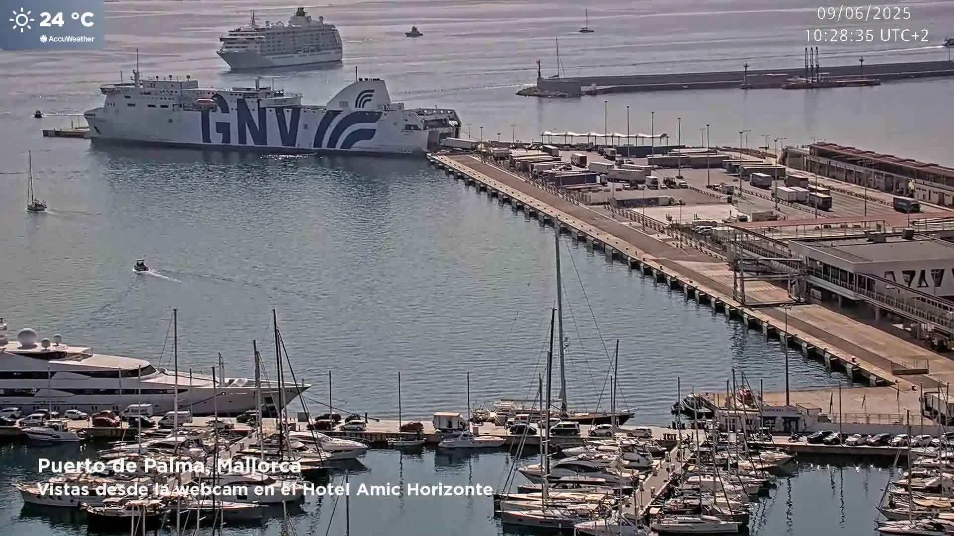 A ferry is docked at a port filled with numerous yachts and sailboats under sunny skies, with a larger cruise ship visible further out in the water.