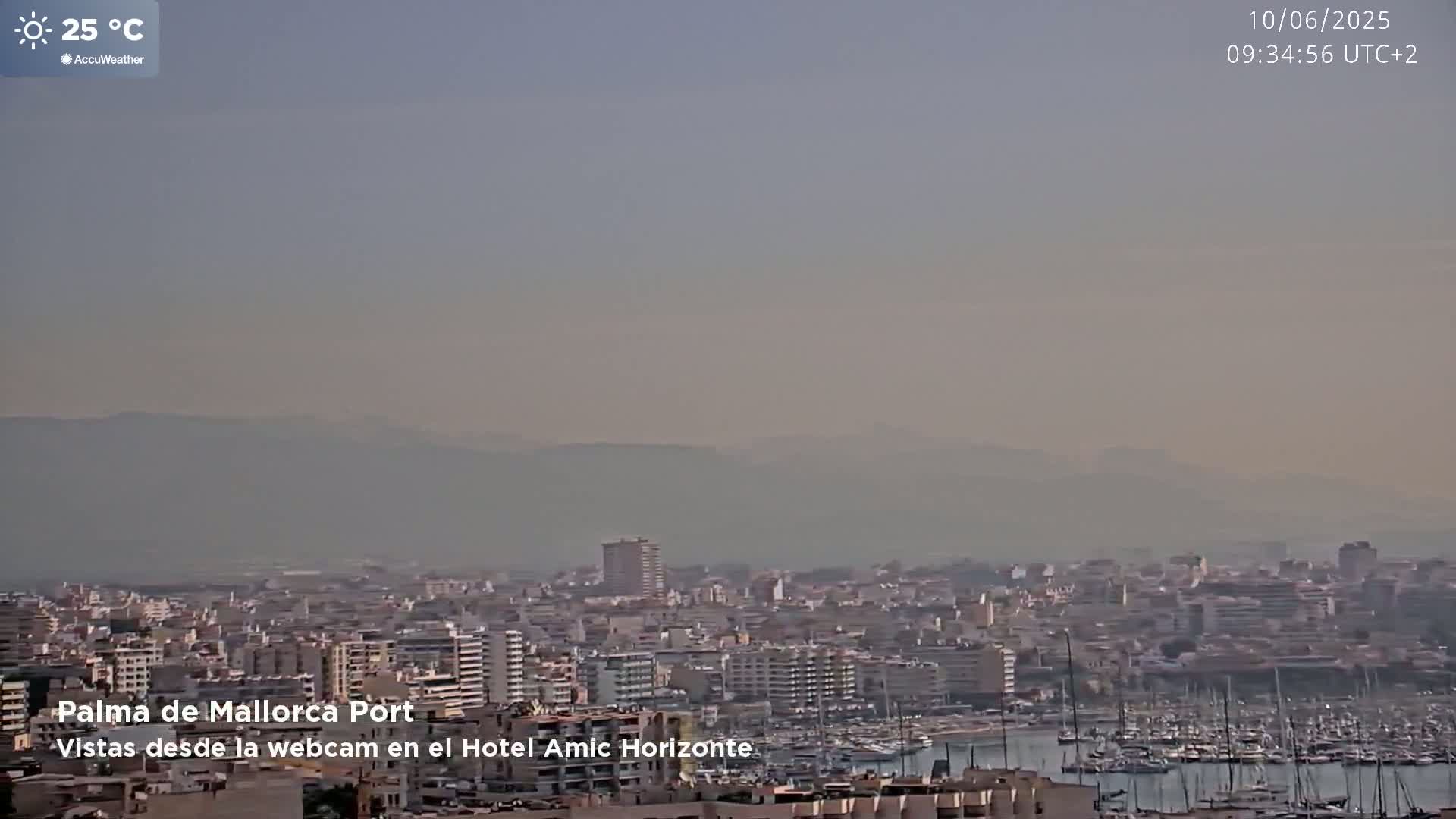 A hazy, sunny view of Palma de Mallorca Port, showing a cityscape with a harbor full of boats and distant mountains.