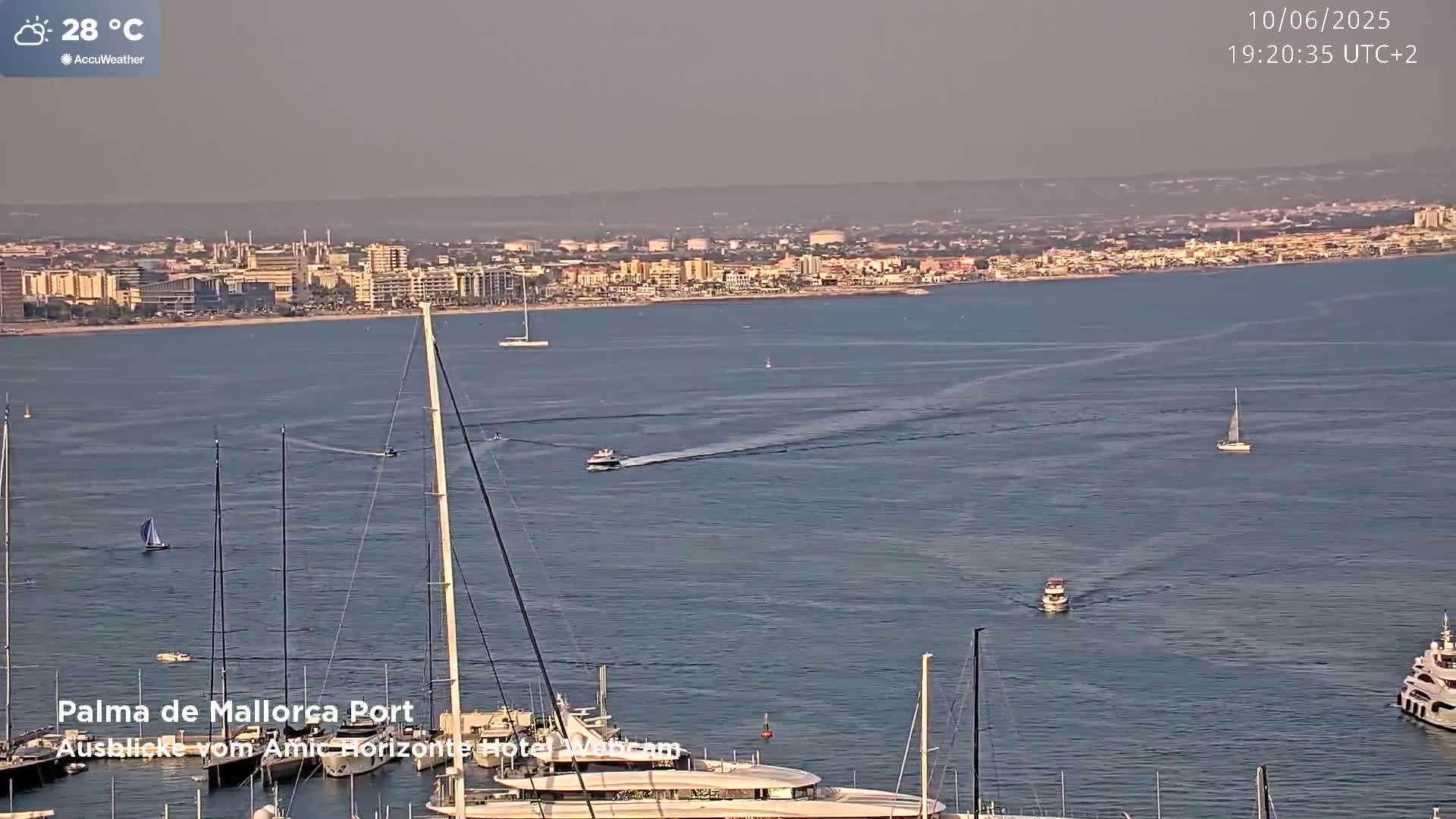 A hazy, sunny harbor scene shows a cityscape across a calm body of water with several sailboats and motorboats, at 28°C.
