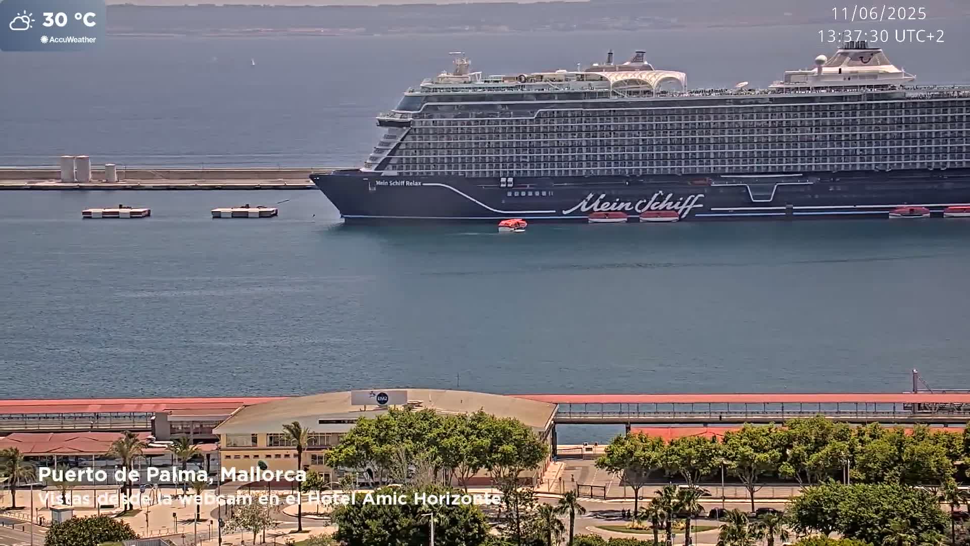 A large cruise ship is docked at a port on a sunny day with calm water and a temperature of 30 degrees Celsius.