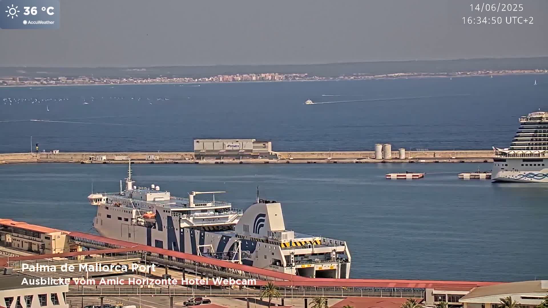 A large ferry is docked at a port on a calm, sunny day with a 36°C temperature, and a cruise ship is visible further out in the harbor.