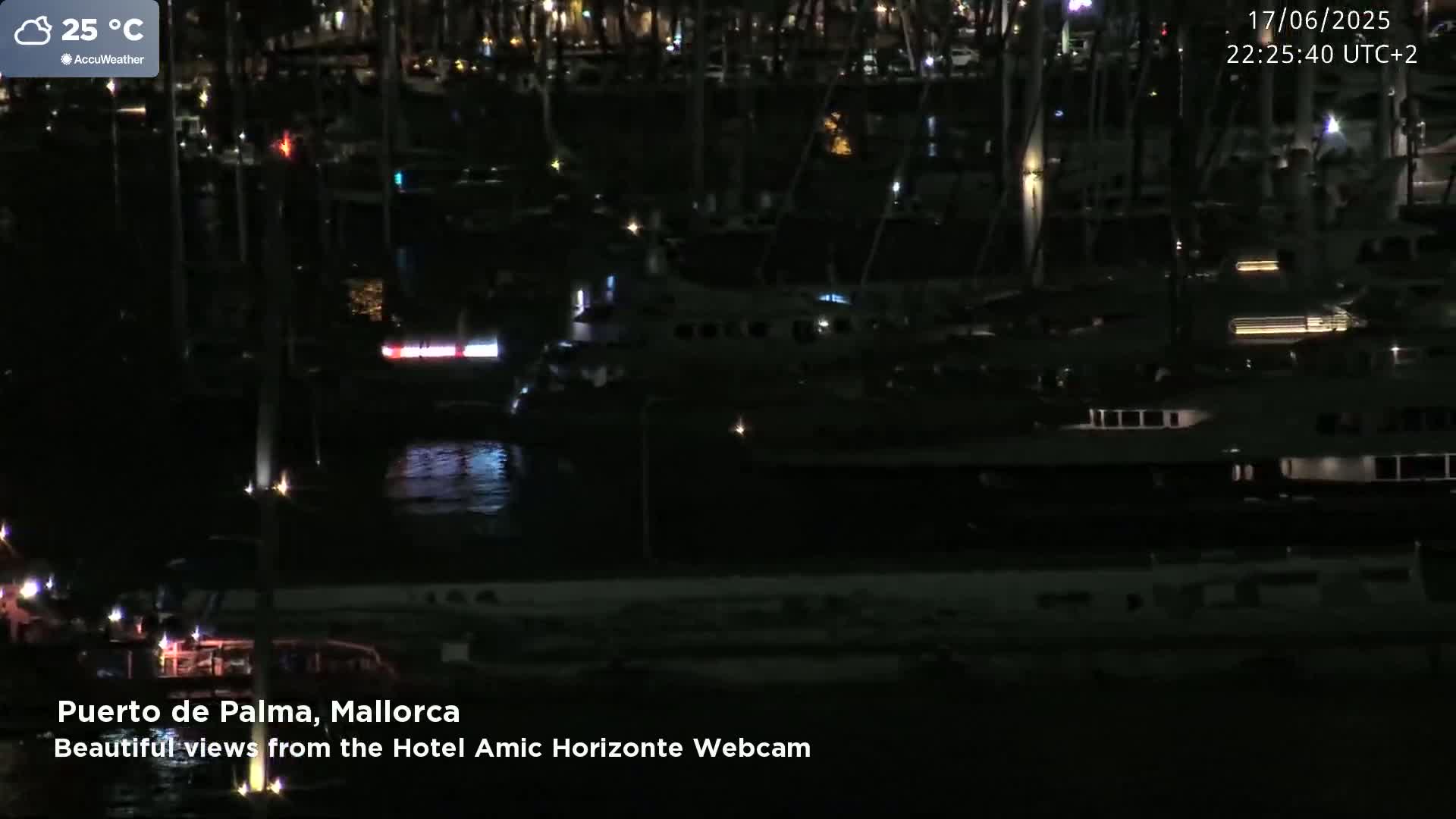A nighttime view of a harbor filled with numerous boats and yachts under a partly cloudy sky, with a temperature of 25 degrees Celsius.