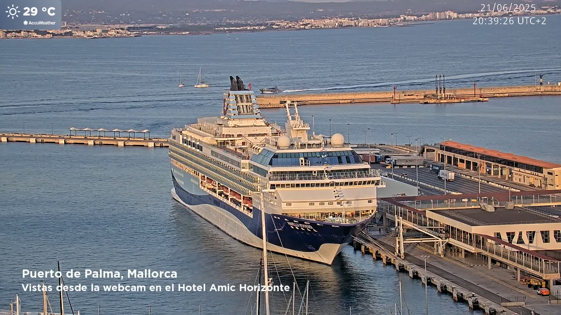 A large cruise ship is docked at a port on a calm, sunny day with a temperature of 29 degrees Celsius.