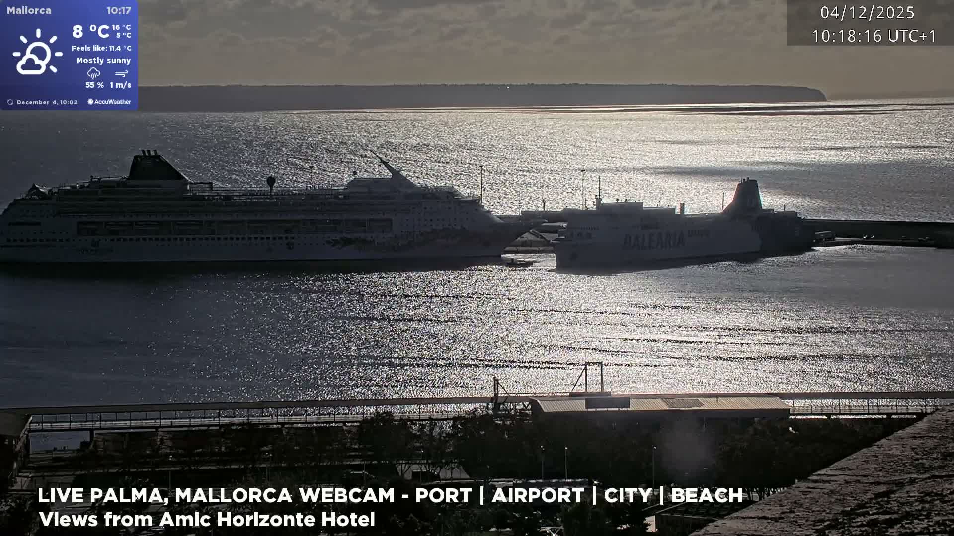 A large cruise ship and a ferry are docked in a bright harbor, with intense sunlight glinting off the water under a hazy, muted sky.
