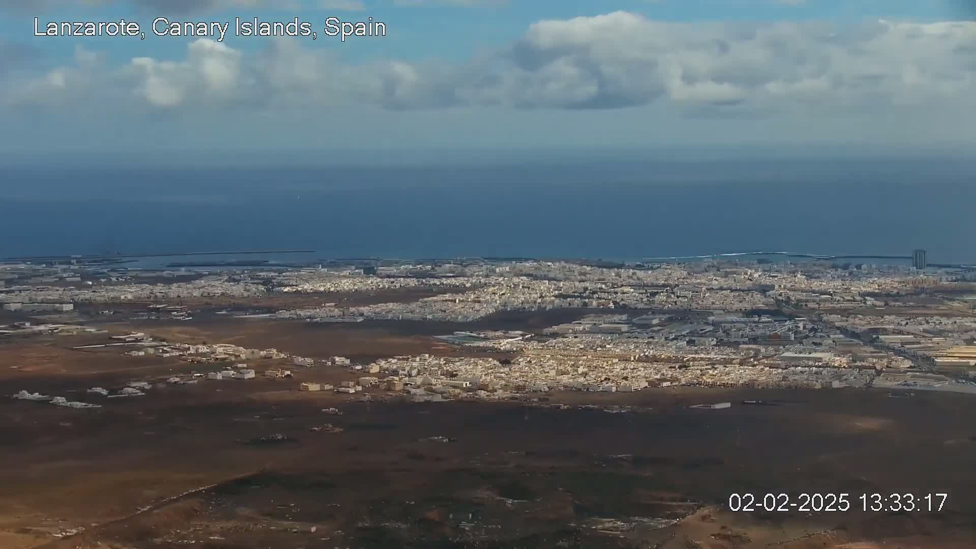 A high-angle view shows a sprawling city next to a dark-blue ocean under a partly cloudy sky.