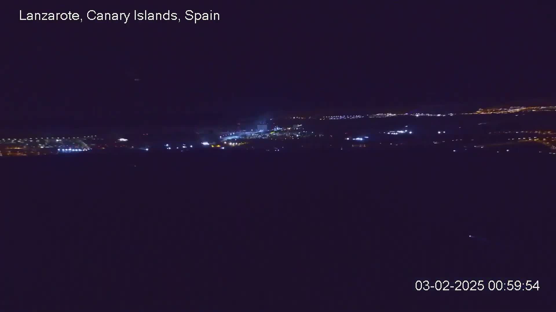 A nighttime, long shot of a city illuminated with scattered lights under a clear, dark sky.
