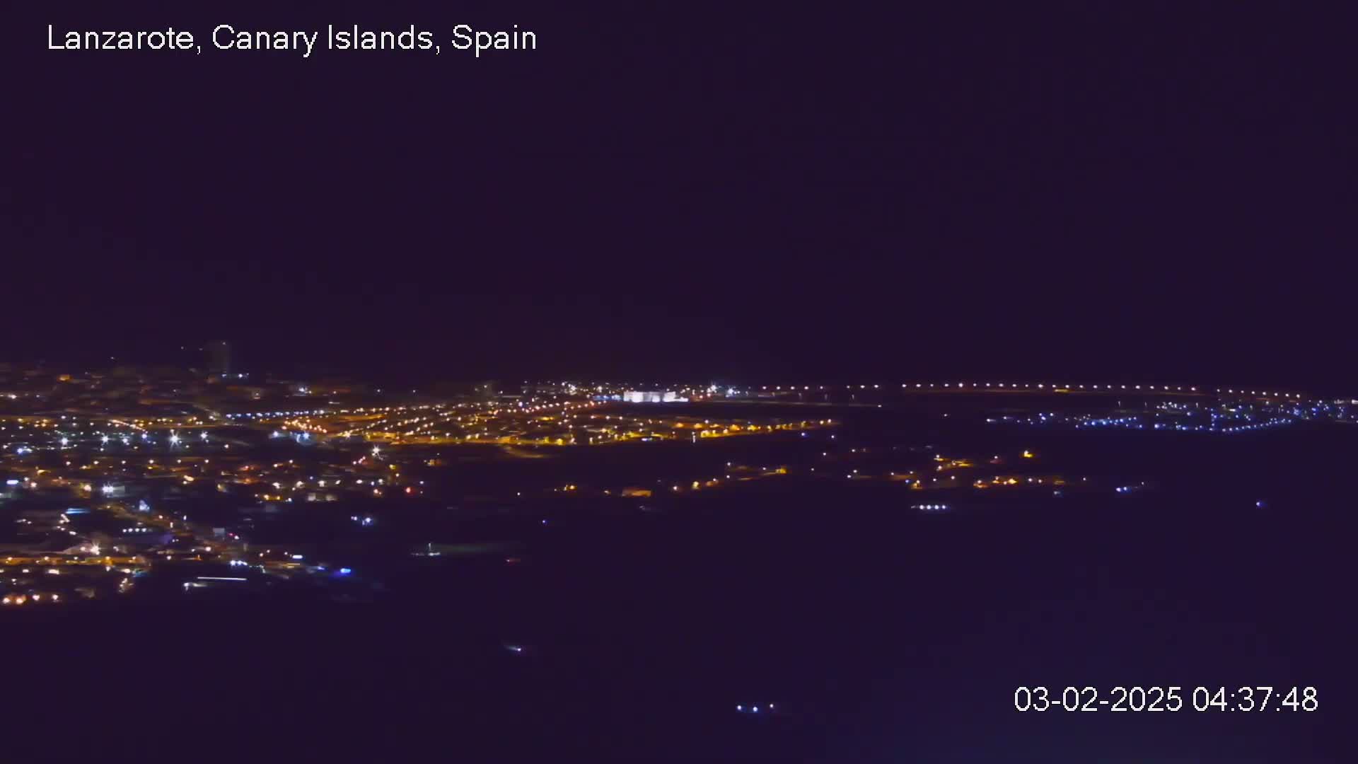 A nighttime, long-distance view of a town with scattered lights under a dark, clear sky.