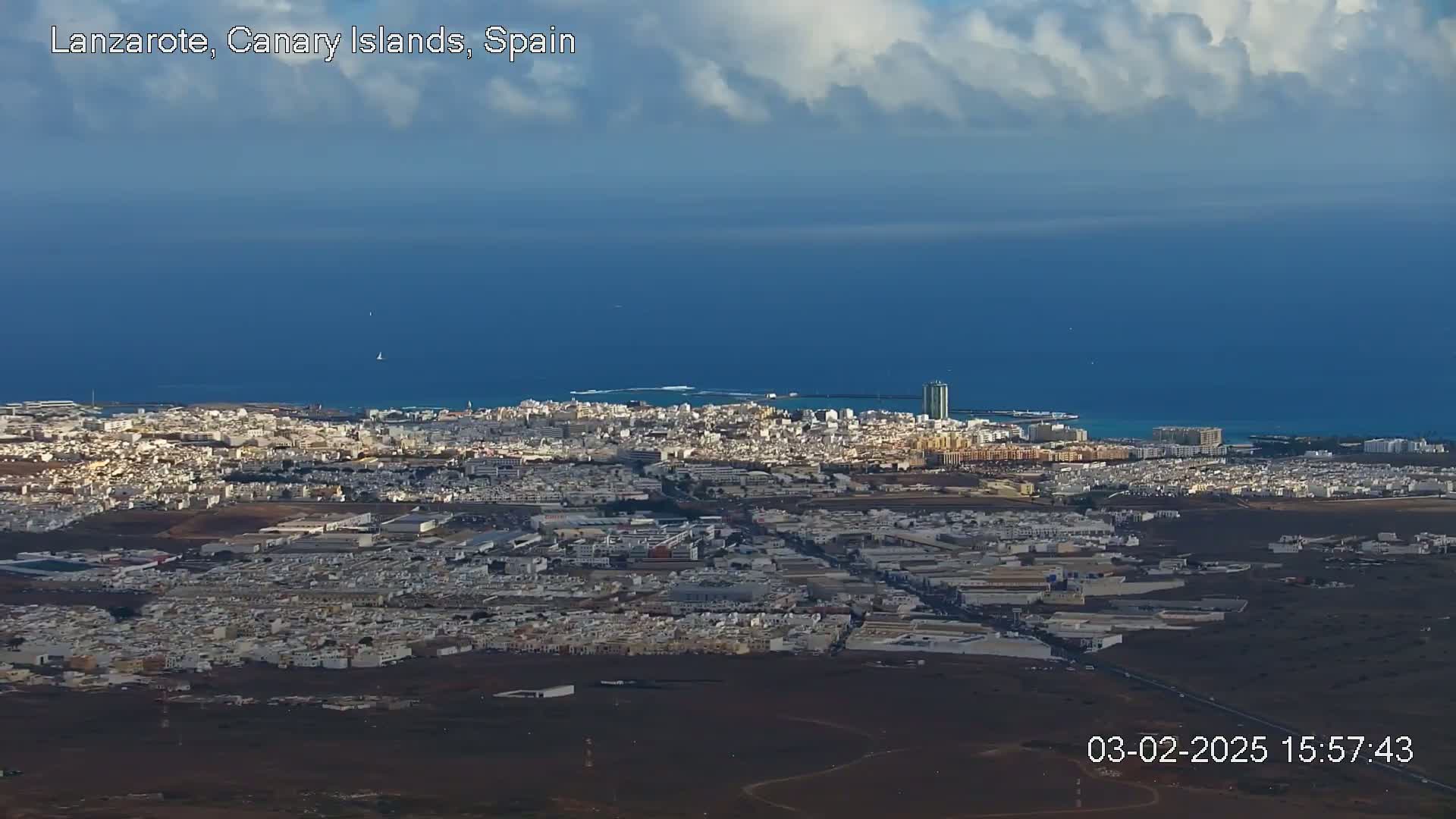 An expansive coastal city with light-colored buildings stretches to a deep blue ocean under a partly cloudy sky.