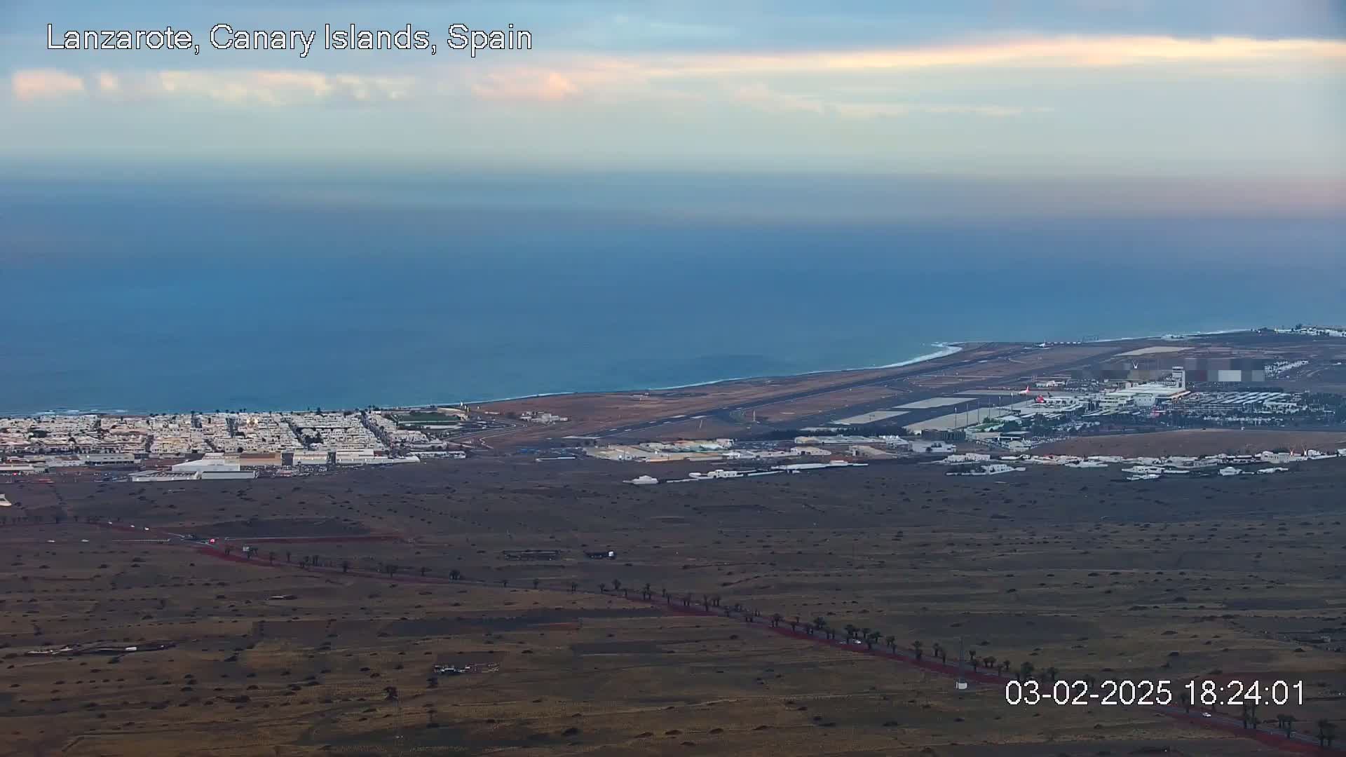 An aerial view of an airport situated on a coastline, with a town nearby, under a partly cloudy twilight sky.