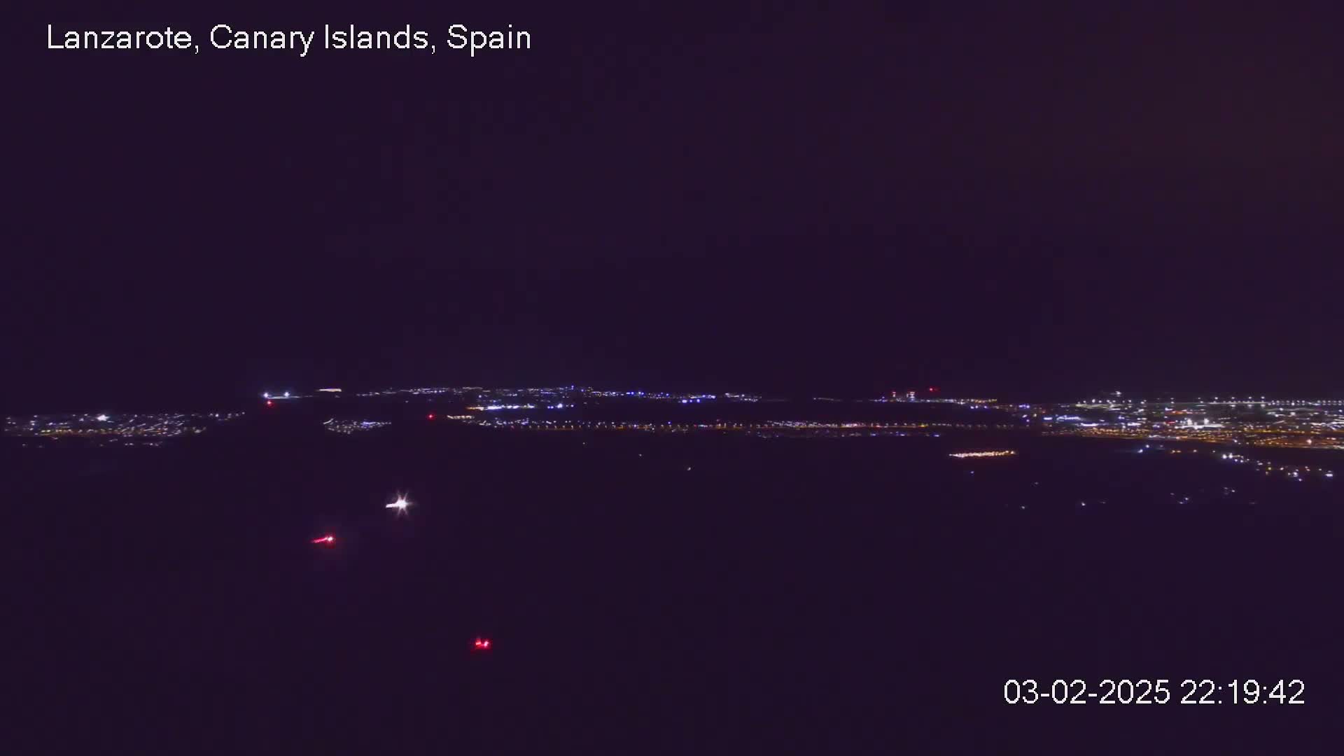 A nighttime long shot shows a distant city skyline illuminated with faint lights under a dark, clear sky.