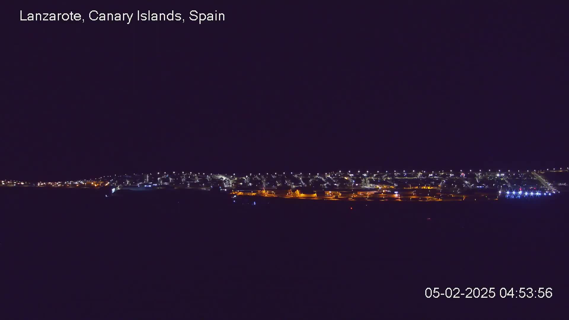 A nighttime long shot shows a city skyline illuminated by many small lights under a clear, dark sky.